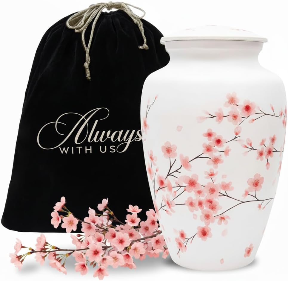White urn with cherry blossom design next to a black drawstring bag with 'Always With Us' text, surrounded by pink flowers.